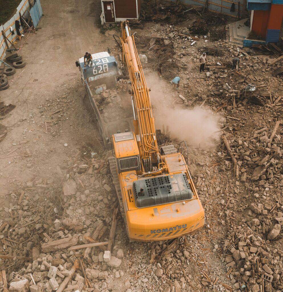 Aerial view of an excavator loading debris at a construction site with workers nearby.